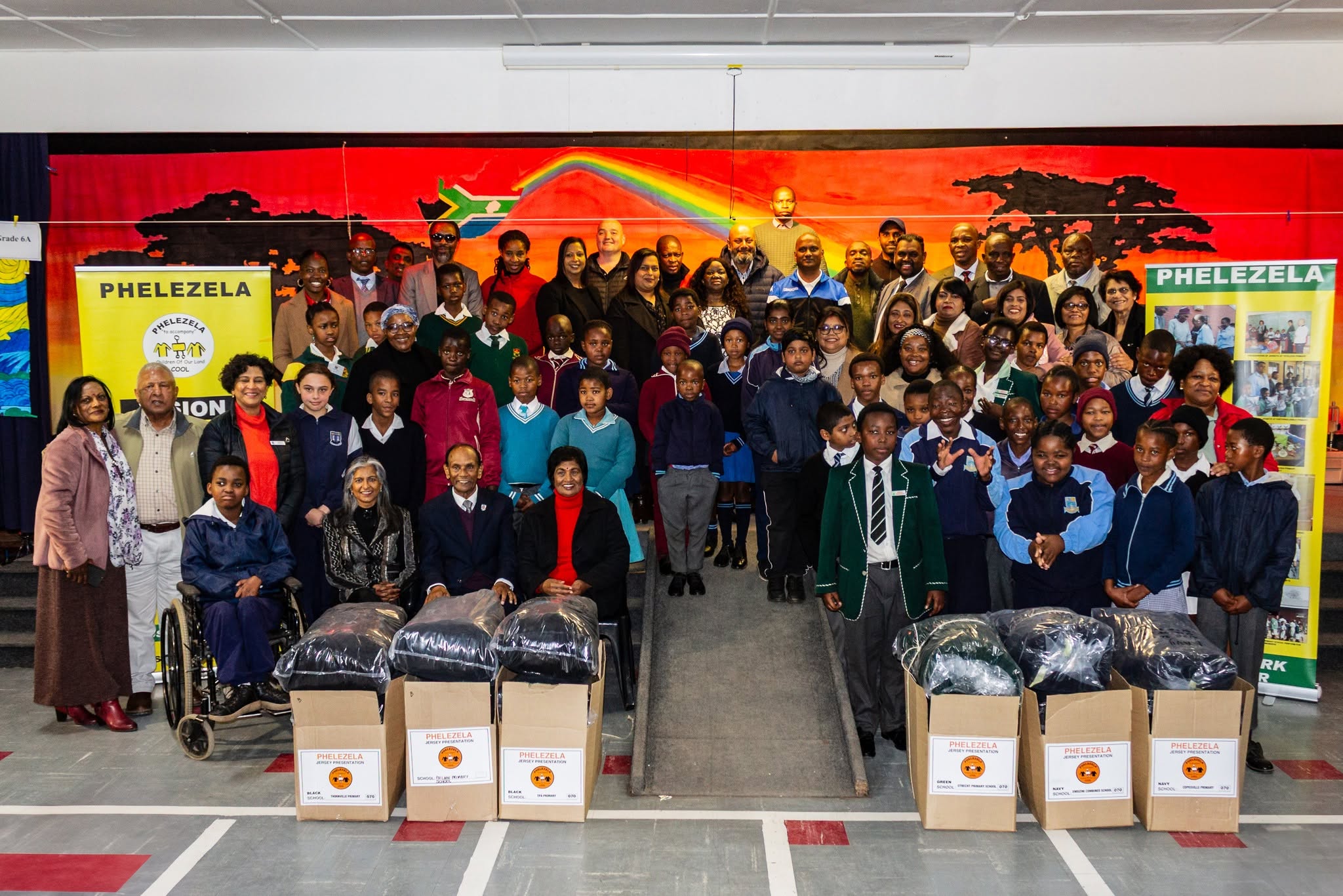 School children in uniform and Phelezela committee members gathered in a school hall with boxes of new jerseys at the 2025 Jersey Presentation